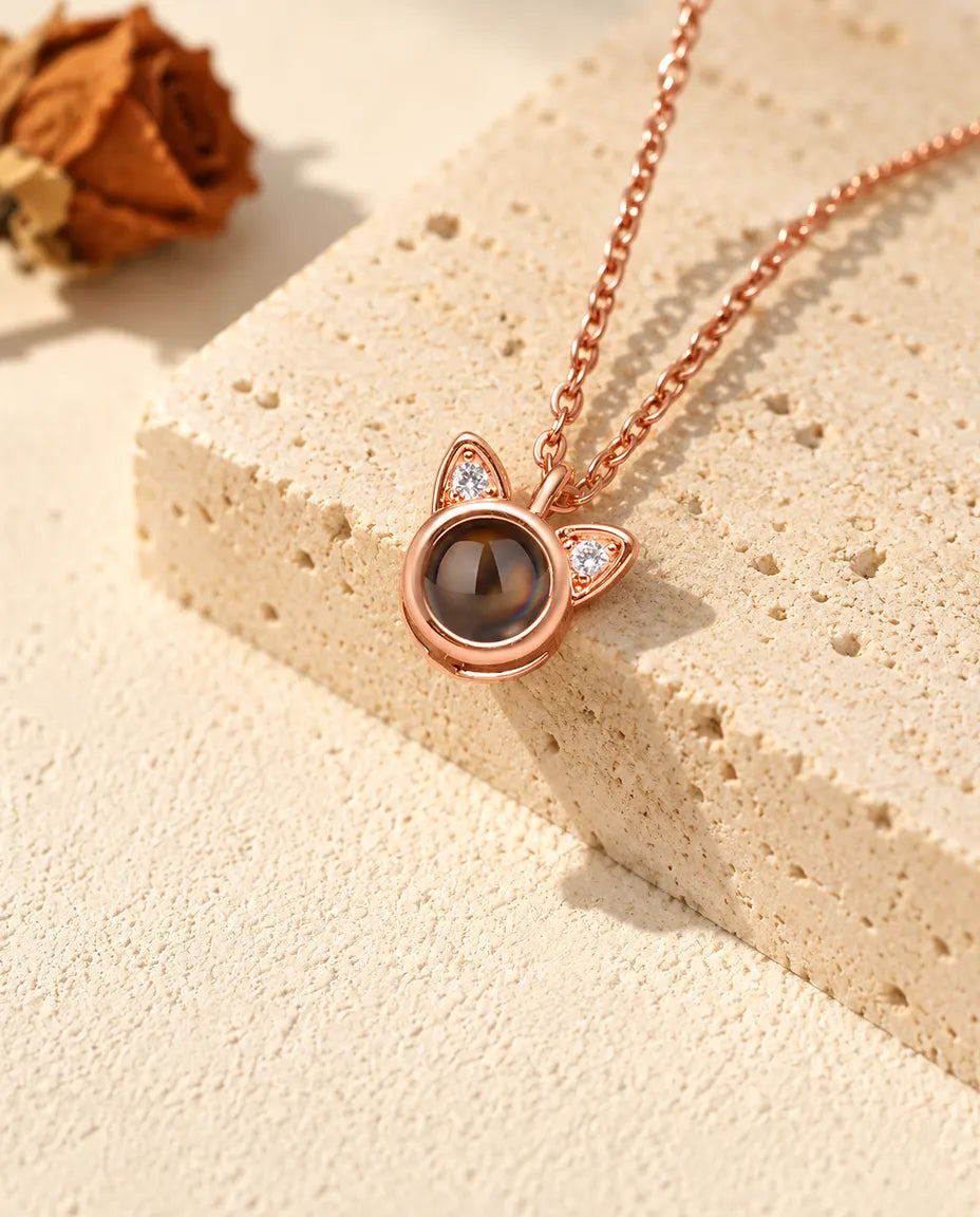Collana con orecchie di gatto color oro rosa appesa davanti a un blocco di travertino