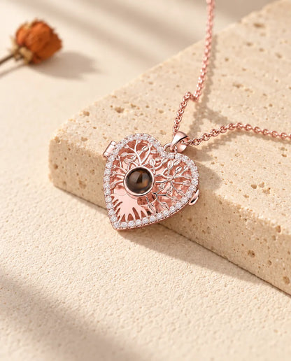 Collana portafoto color oro rosa a cuore albero della vita adagiata su un blocco di travertino