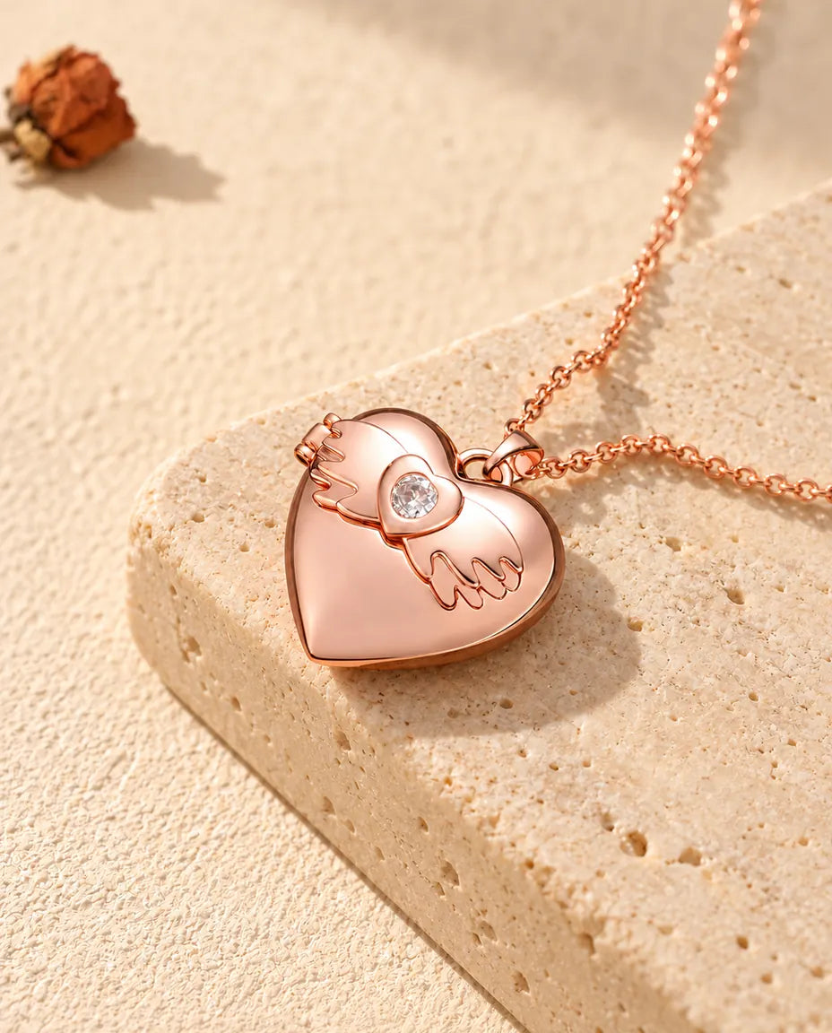 Collana portafoto a cuore con ali d'angelo color oro rosa sul travertino, alla luce calda del sole