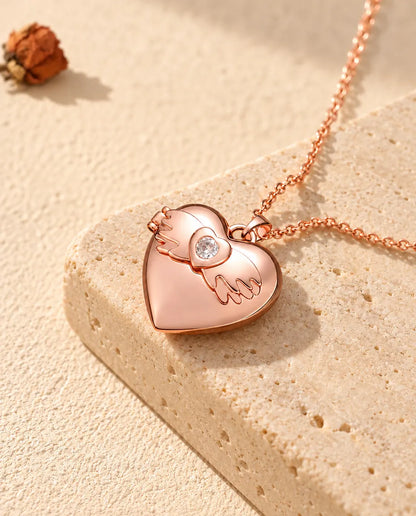 Collana portafoto a cuore con ali d'angelo color oro rosa sul travertino, alla luce calda del sole