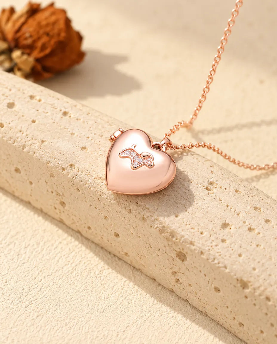Collana portafoto a cuore con cagnolino color oro rosa sul travertino, alla luce calda del sole