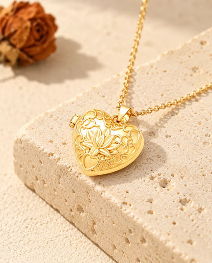 Collana portafoto dorata a cuore con fiore di loto, appoggiata su un blocco di travertino