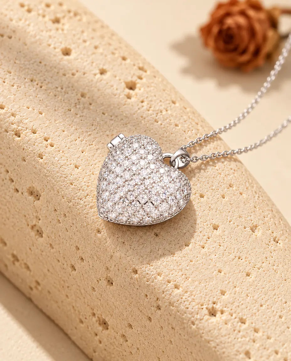 Collana portafoto a cuore pavé argentata, con il coperchio tutto di zirconi, appoggiata a un blocco di travertino