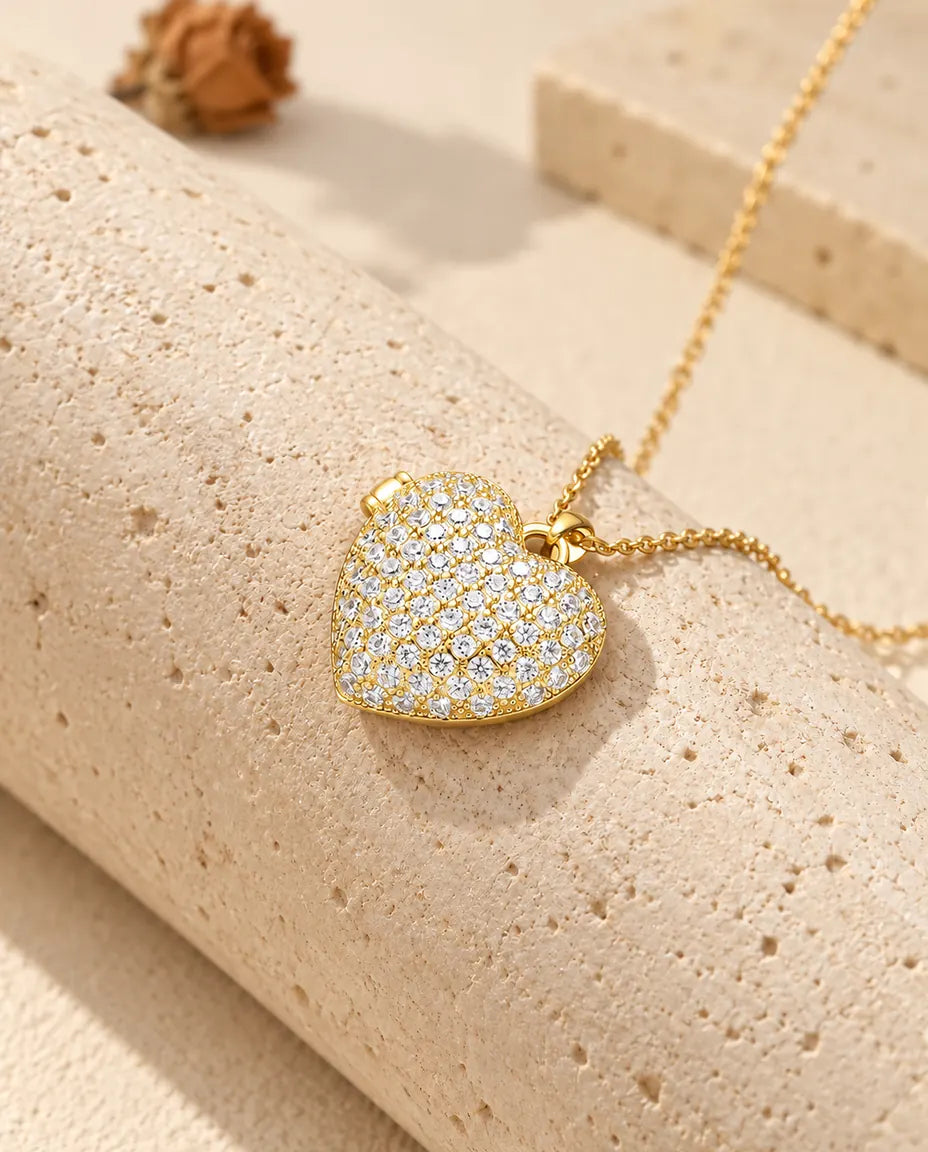 Collana portafoto a cuore pavé dorata appoggiata a un blocco di travertino