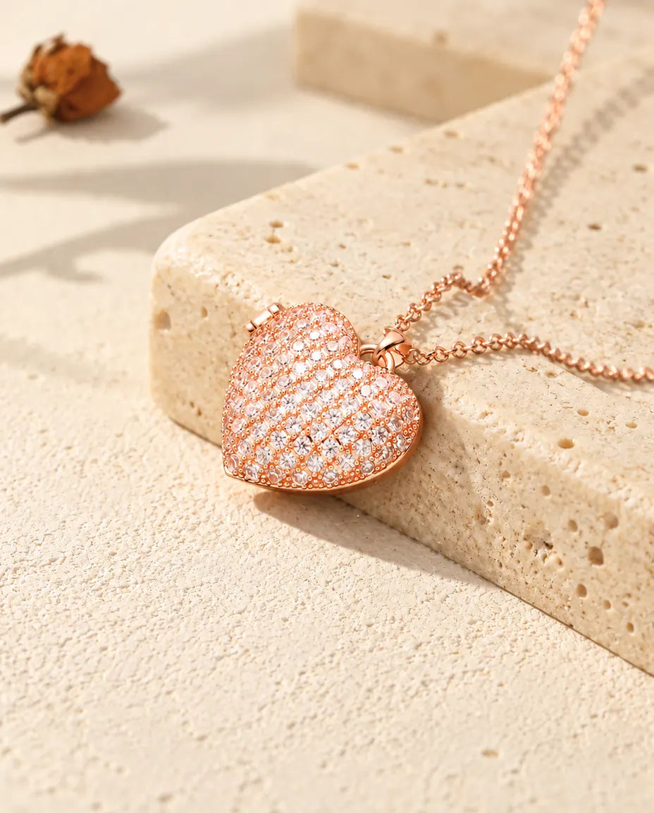 Collana portafoto a cuore pavé color oro rosa sul travertino, alla luce calda del sole