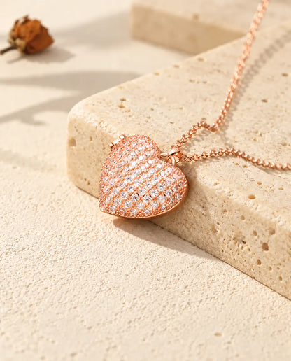 Collana portafoto a cuore pavé color oro rosa sul travertino, alla luce calda del sole