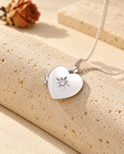 Collana portafoto a cuore satinato con fiore argentata con un fiorellino e uno zircone appoggiata a un blocco di travertino