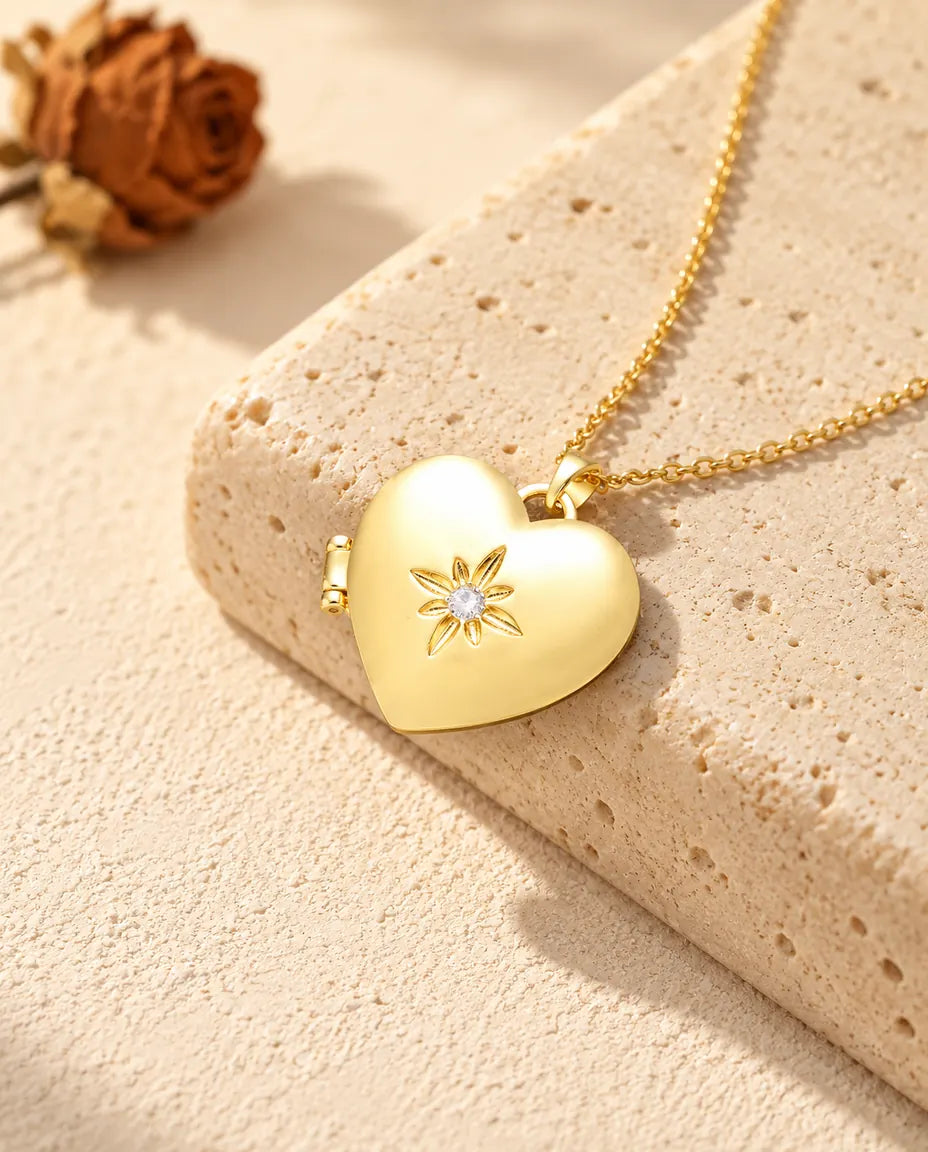 Collana portafoto a cuore satinato con fiore dorata appoggiata a un blocco di travertino