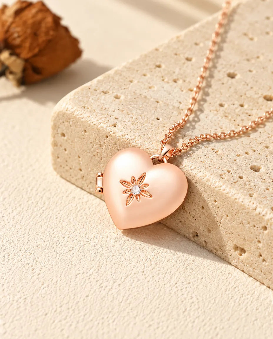 Collana portafoto a cuore satinato con fiore color oro rosa sul travertino, alla luce calda del sole