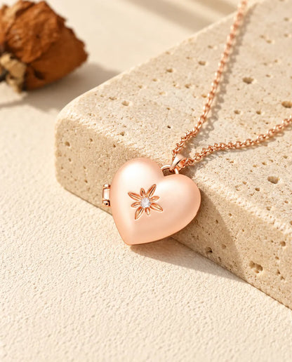 Collana portafoto a cuore satinato con fiore color oro rosa sul travertino, alla luce calda del sole