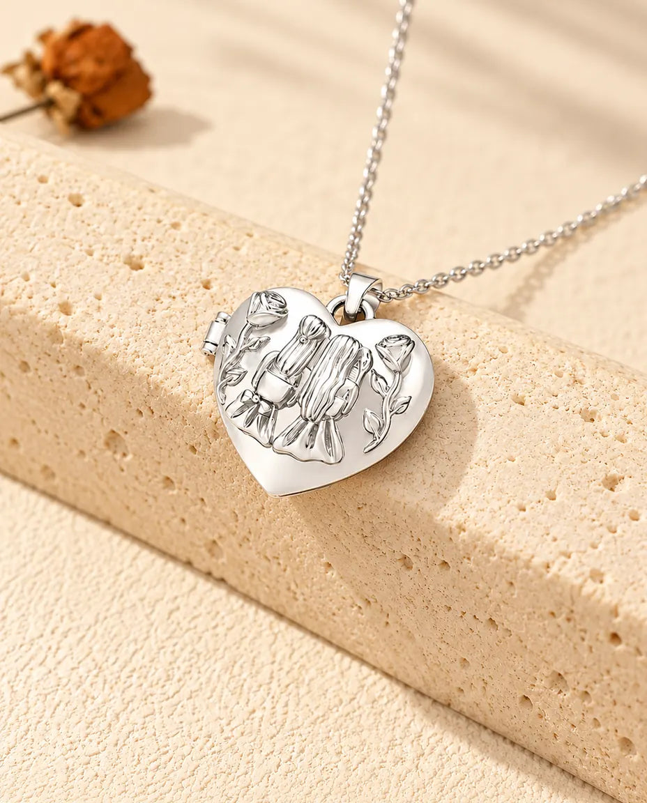 Collana portafoto argentata a cuore Sorelle con due ragazze e rose sul coperchio, appoggiata su un blocco di travertino