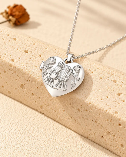 Collana portafoto argentata a cuore Sorelle con due ragazze e rose sul coperchio, appoggiata su un blocco di travertino