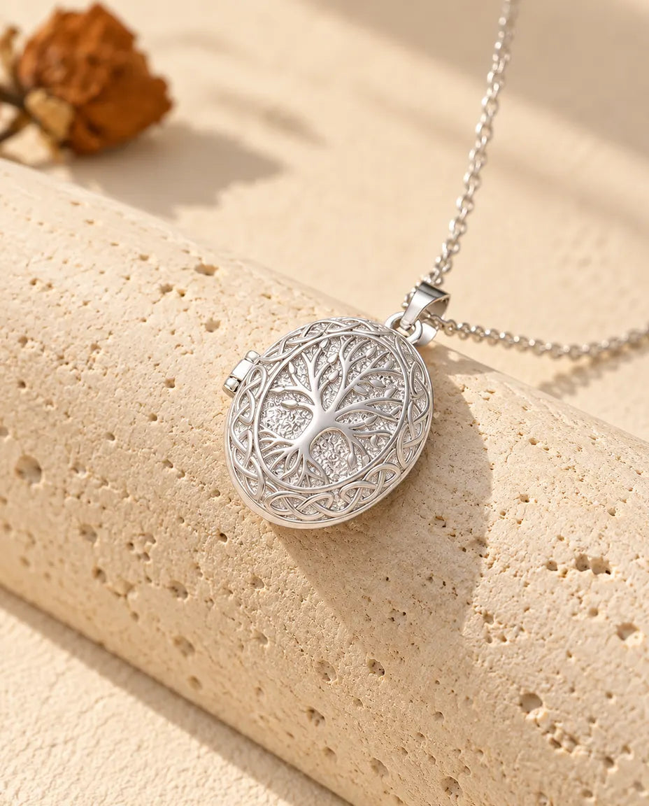 Collana portafoto ovale argentata con albero della vita e bordo a nodi celtici, adagiata su un blocco di travertino