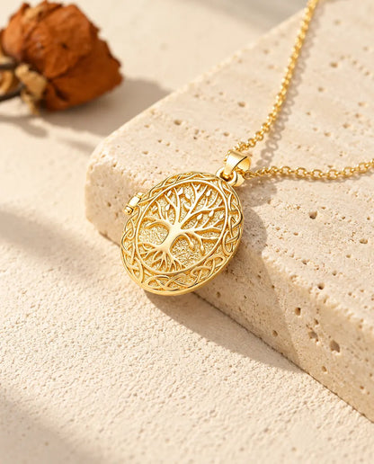 Collana portafoto ovale dorata con albero della vita appoggiata sul bordo di un blocco di travertino