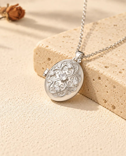 Collana portafoto ovale personalizzata argentata, con fiore in filigrana e zirconi, appoggiata su un blocco di travertino