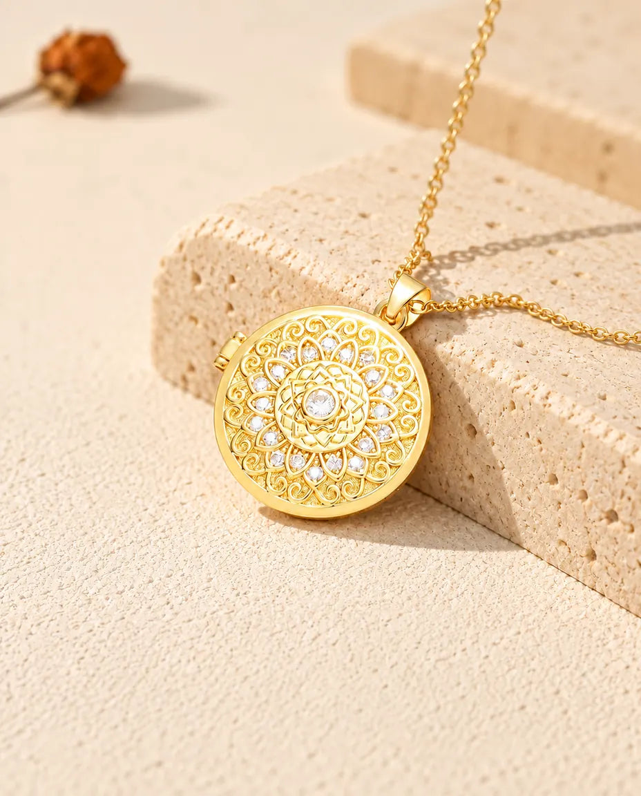 Collana portafoto dorata tonda con fiore mandala e zirconi, appoggiata su un blocco di travertino