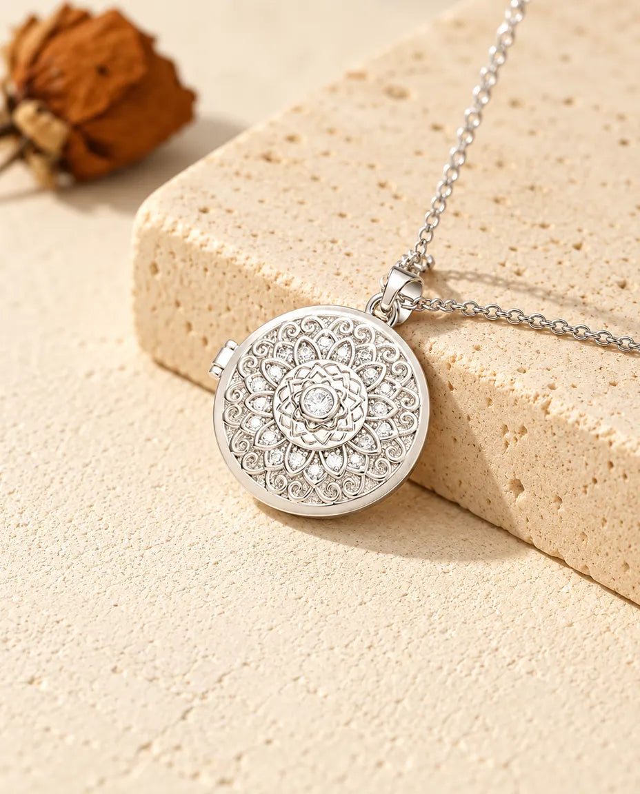 Collana portafoto argentata tonda con fiore mandala e petali di zirconi, appoggiata su un blocco di travertino