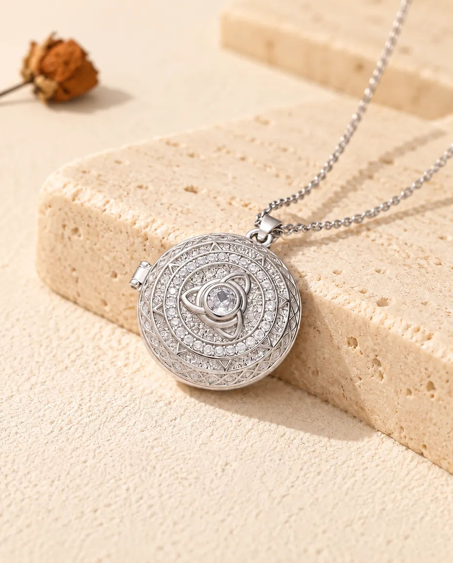 Collana portafoto tonda argentata con triquetra celtica e zirconi, appoggiata su un blocco di travertino