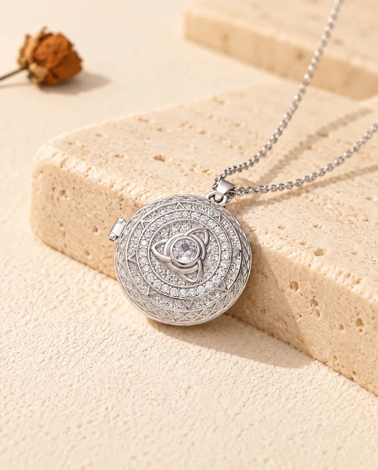 Collana portafoto tonda argentata con triquetra celtica e zirconi, appoggiata su un blocco di travertino
