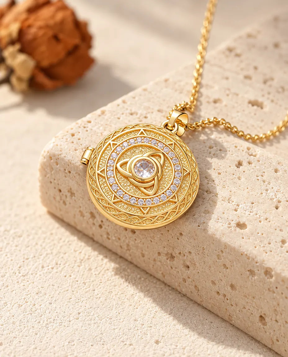 Collana portafoto tonda dorata con triquetra e zircone centrale adagiata su un blocco di travertino