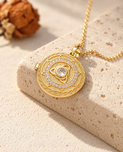 Collana portafoto tonda dorata con triquetra e zircone centrale adagiata su un blocco di travertino