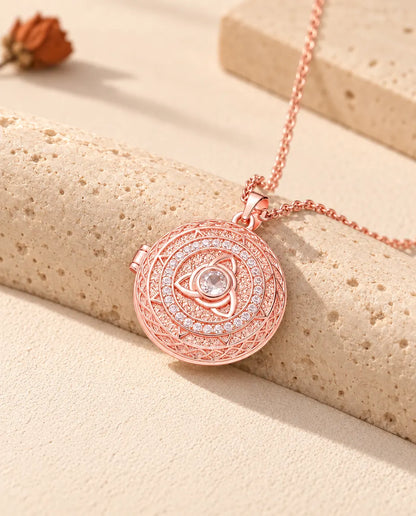 Ciondolo portafoto color oro rosa con triquetra e cerchio di zirconi posato sul travertino