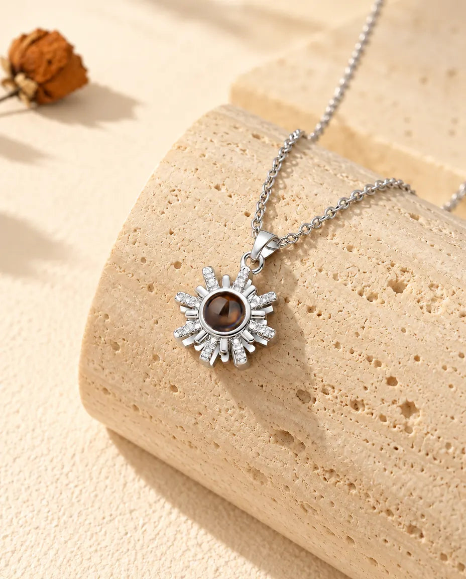 Collana argentata a forma di sole con foto dentro appesa davanti a un blocco di travertino