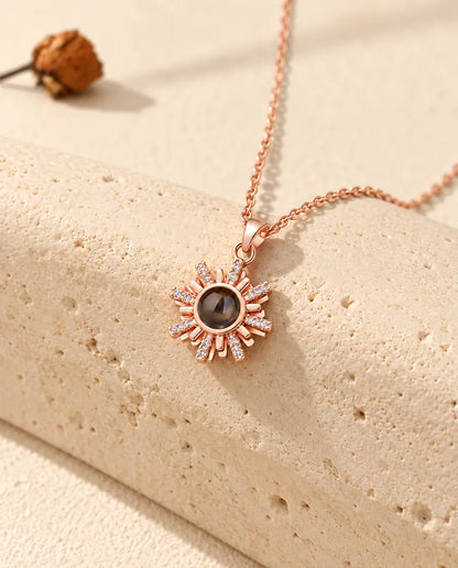 Collana color oro rosa a forma di sole con foto dentro appesa davanti a un blocco di travertino