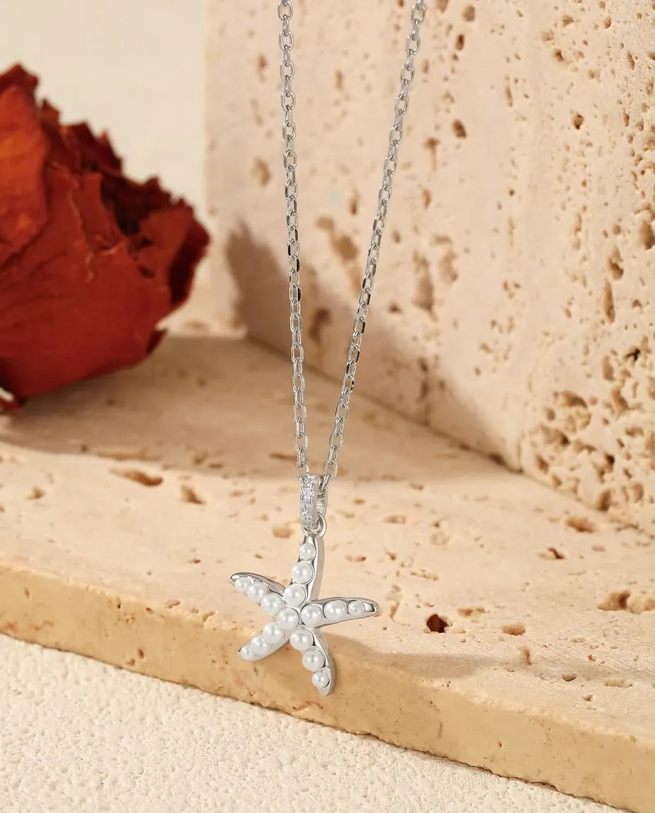 Collana Stella Marina in Argento 925 - ciondolo appeso al bordo di una lastra di travertino