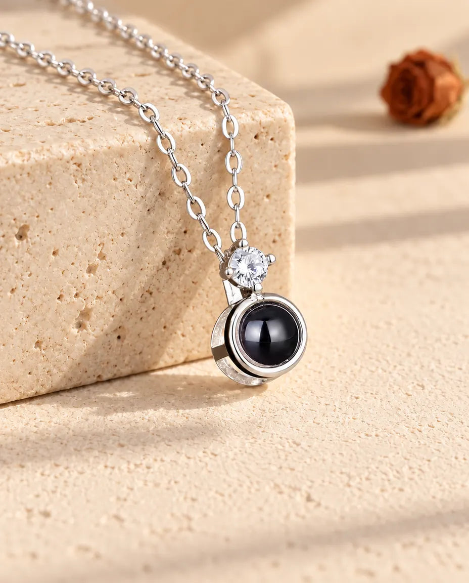 Collana argentata con punto luce e foto dentro distesa su un blocco di travertino