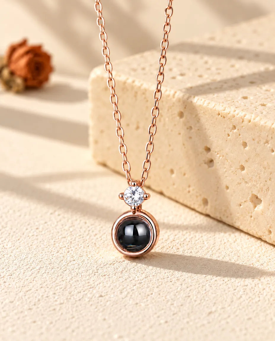 Collana color oro rosa con punto luce e foto dentro appesa davanti a un blocco di travertino