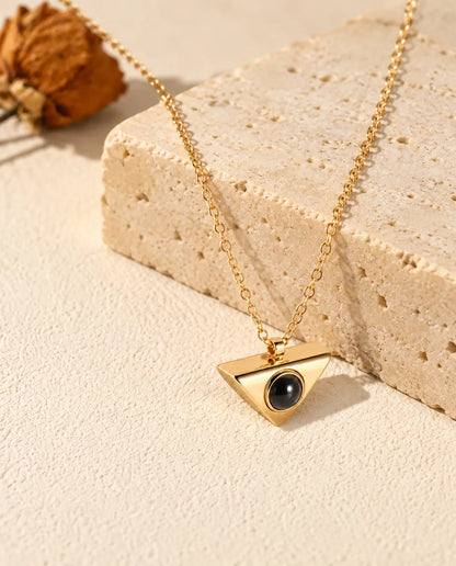 Collana dorata a triangolo con foto dentro appesa davanti a un blocco di travertino