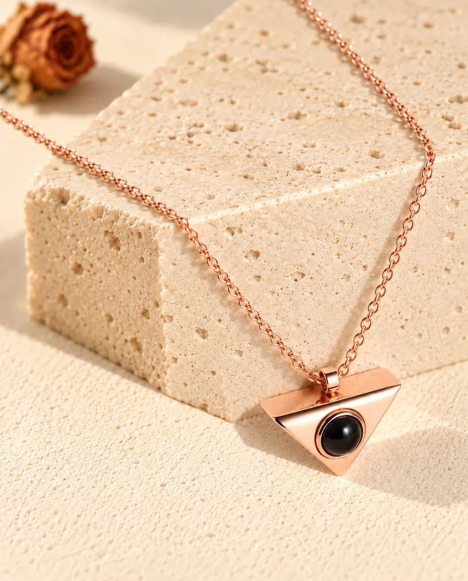 Collana color oro rosa a triangolo con foto dentro appesa davanti a un blocco di travertino