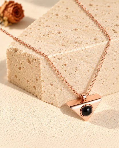 Collana color oro rosa a triangolo con foto dentro appesa davanti a un blocco di travertino