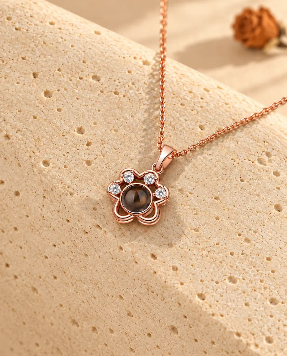 Collana a zampa color oro rosa con foto dentro appesa sopra il travertino