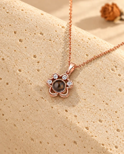 Collana a zampa color oro rosa con foto dentro appesa sopra il travertino