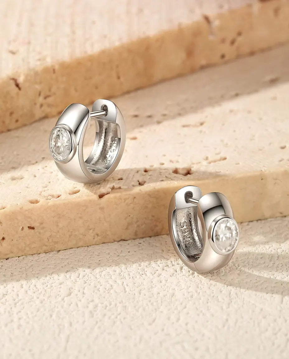 Orecchini a Cerchio Huggie con Moissanite Ovale in Argento 925 - la coppia su gradini di travertino