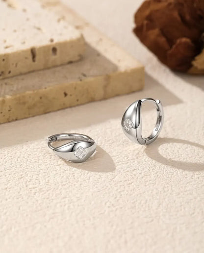 Orecchini a Cerchio Huggie Moissanite Asscher in Argento 925 - la coppia su una superficie chiara ruvida, uno disteso e uno in piedi