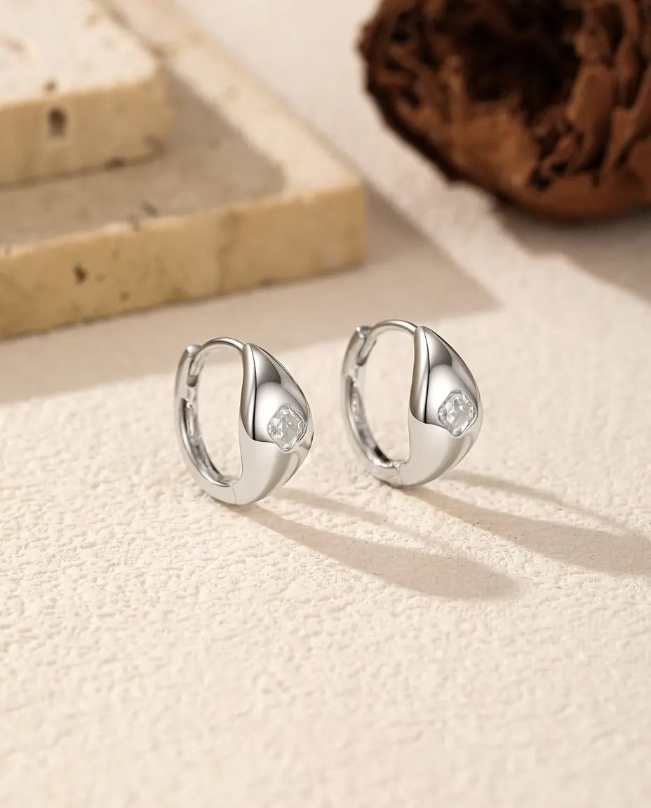 Orecchini a Cerchio Huggie Moissanite Asscher in Argento 925 - la coppia affiancata su una superficie chiara ruvida