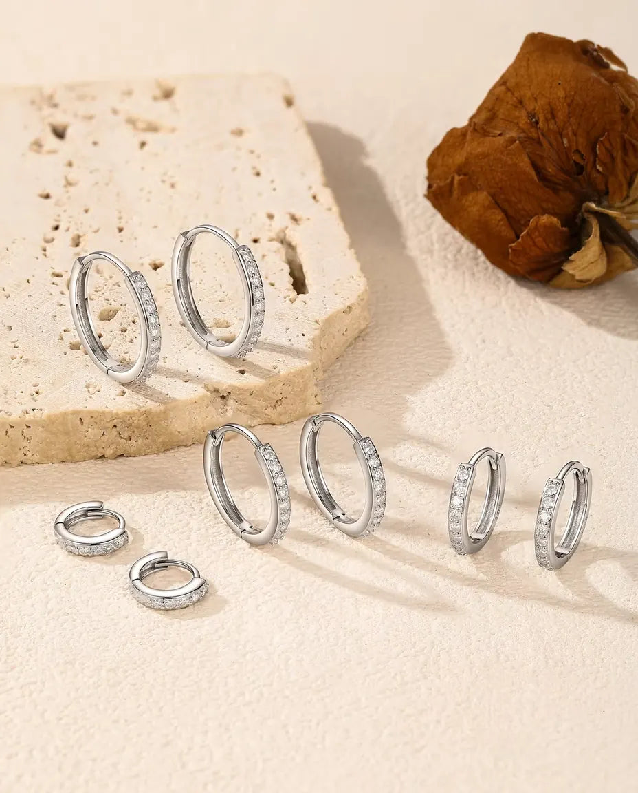 Orecchini a Cerchio Moissanite in Argento 925 - tutte e cinque le misure su una superficie chiara accanto a una lastra di travertino