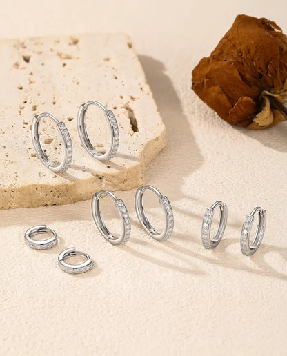 Orecchini a Cerchio Moissanite in Argento 925 - tutte e cinque le misure su una superficie chiara accanto a una lastra di travertino