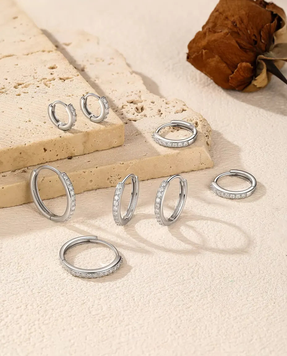 Orecchini a Cerchio Moissanite in Argento 925 - cinque misure sparse su una lastra di travertino e una superficie chiara