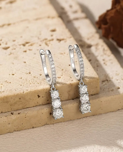 Orecchini a Cerchio Pendenti Moissanite a Tre Pietre in Argento 925 - la coppia appesa al bordo di una lastra di travertino