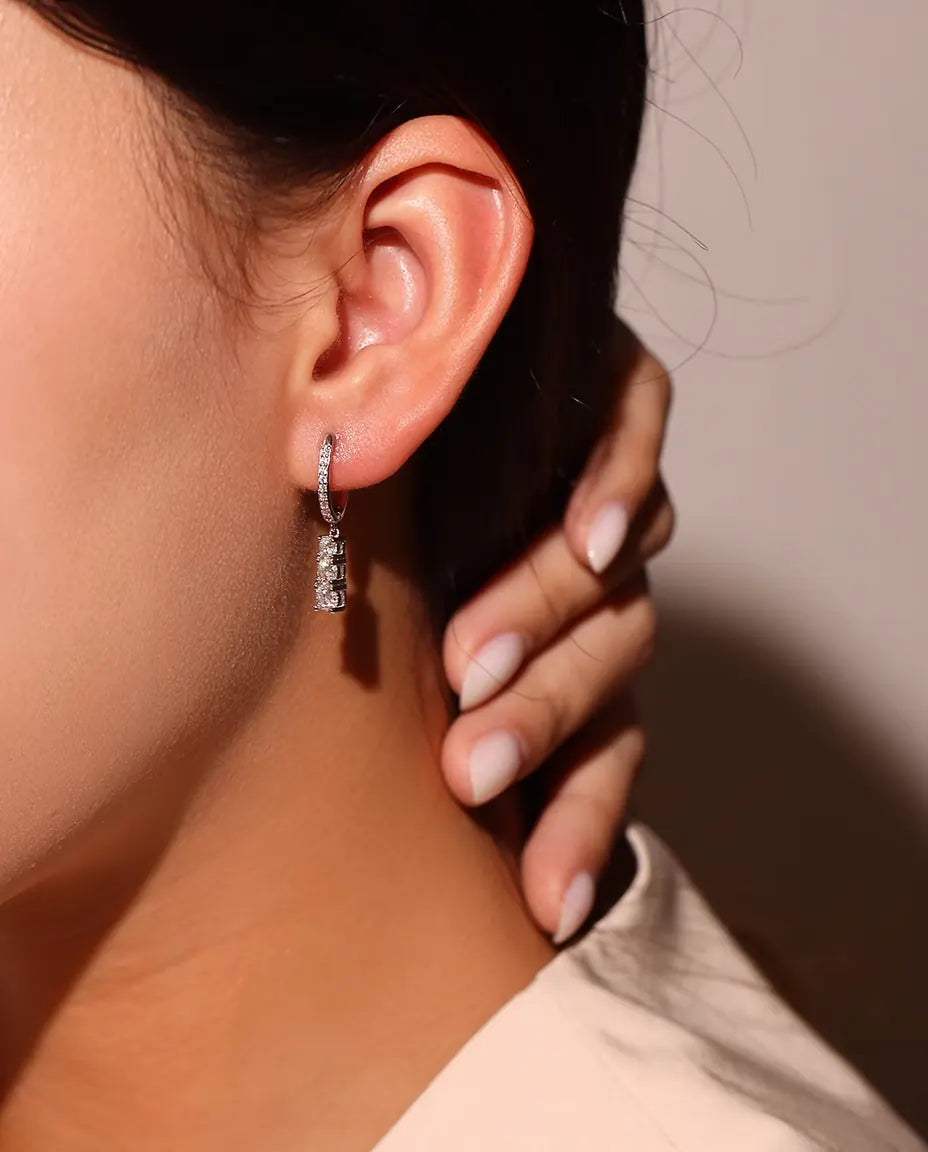 Orecchini a Cerchio Pendenti Moissanite a Tre Pietre in Argento 925 - indossati all’orecchio da una modella, dita sul collo