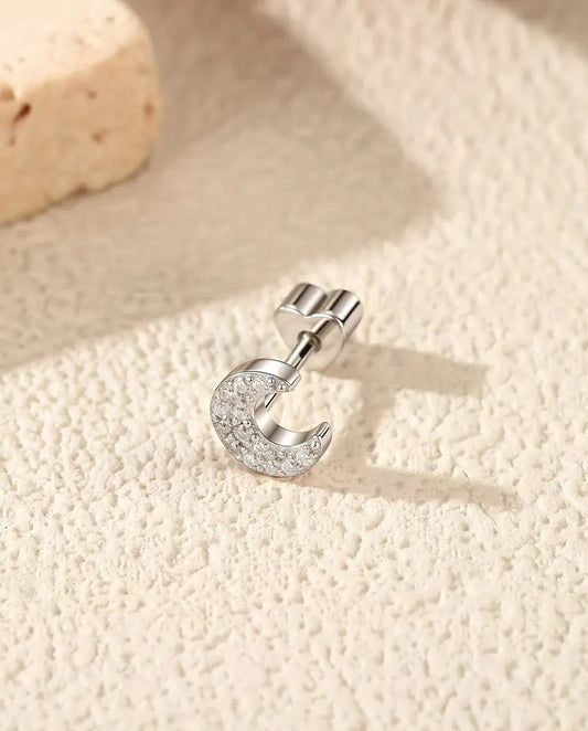 Orecchini a Mezzaluna con Pavé di Moissanite in Argento 925 - appoggiato di lato su una superficie chiara ruvida, chiusura a forma di cuore sul perno
