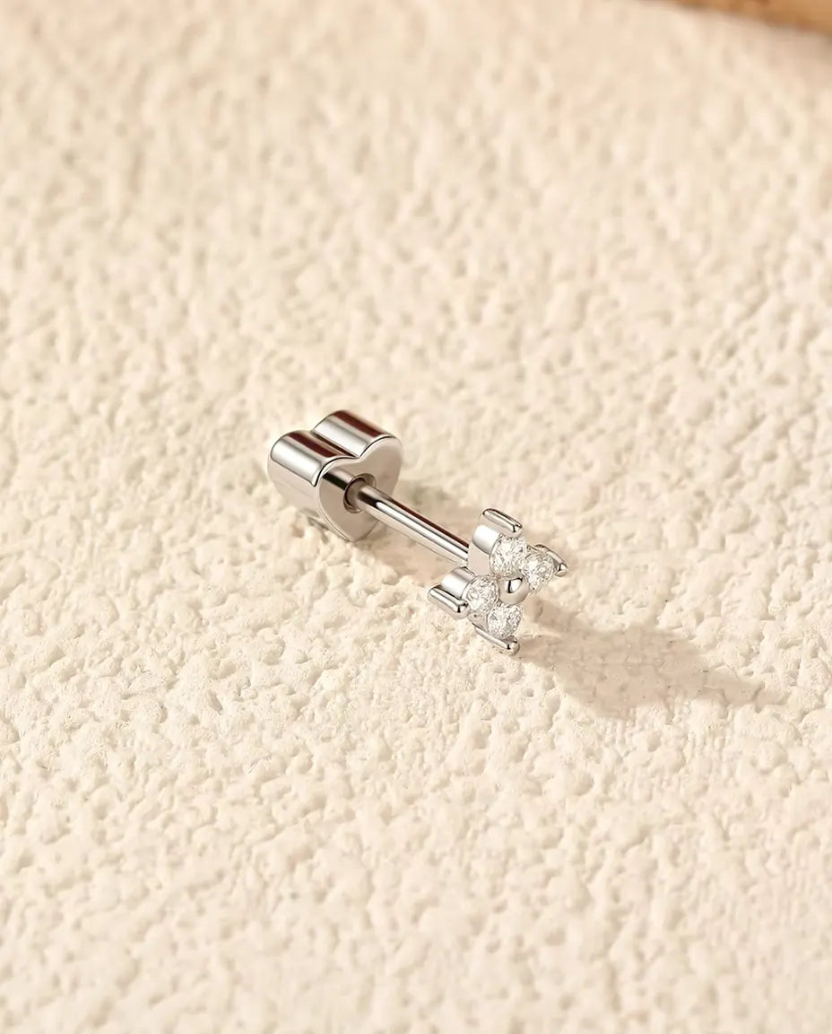 Orecchini a Quadrifoglio con Moissanite in Argento 925 - appoggiato di lato su una superficie chiara ruvida, chiusura a forma di cuore sul perno